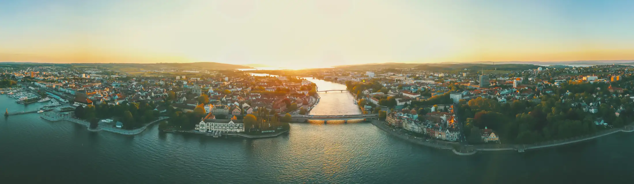 Luftaufnahme Konstanz: links Hafen und Imperia, daneben Altstadt und Paradies, mittig Konstanzer Trichter mit Alter Rheinbrücke Konstanz vorne, dahinter Fahrradbrücke, rechts Petershausen West und Ost, dahinter Industriegebiet. Vordergrund der Bodensee