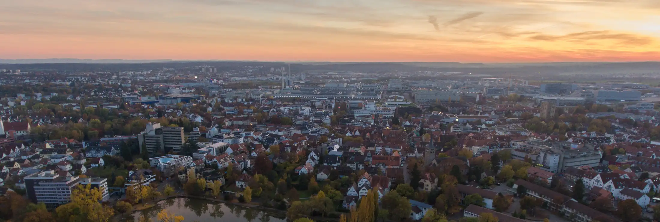 Luftaufnahme Sindelfingen. Vorne: links Klostersee, Immobilien Burghaldenstr., mittig Immobilien Seestr., Martinskirche rechts: Martinsschule, Hallenbad Klostergarten. Dahinter: Mercedes-Benz Hallen, Gebäude südwestliche Kernstadt, rechts: Sonnenuntergang