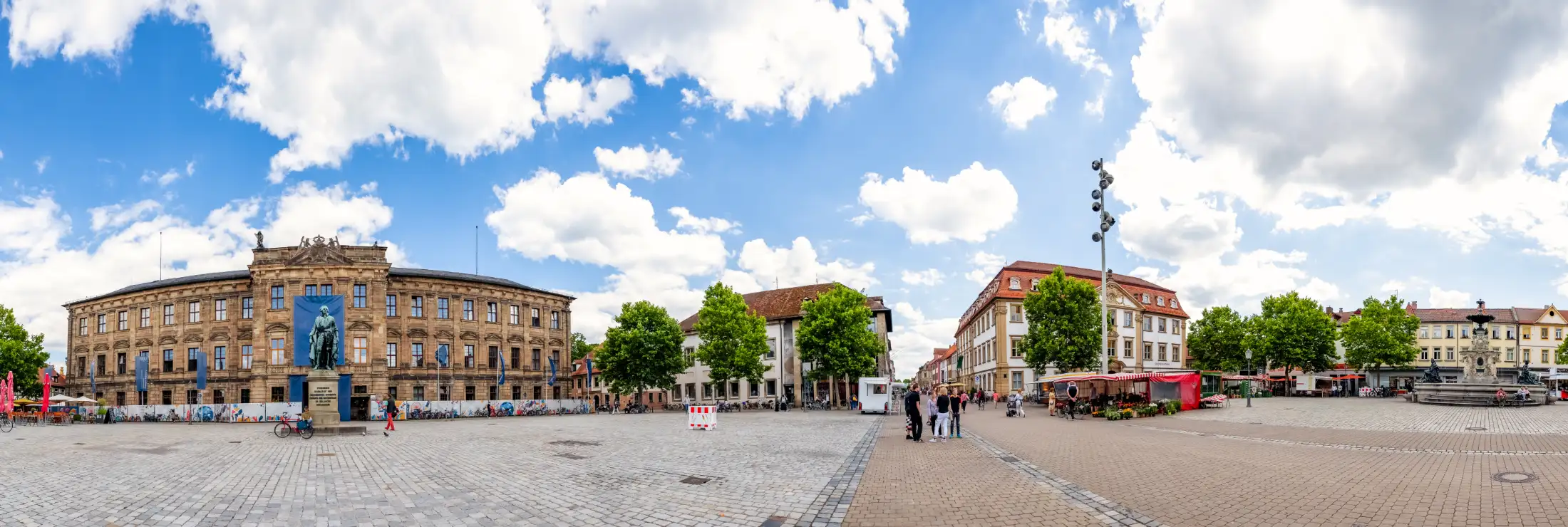 Panoramaaufnahme vom Schloßplatz Erlangen: links Friedrich-Alexander-Universität Erlangen-Nürnberg, davor Standbild Markgraf Friedrich von Brandenburg-Bayreuth, mittig die Immobilien des südlichen Marktplatzes, Palais Stutterheim, ganz rechts Paulibrunnen