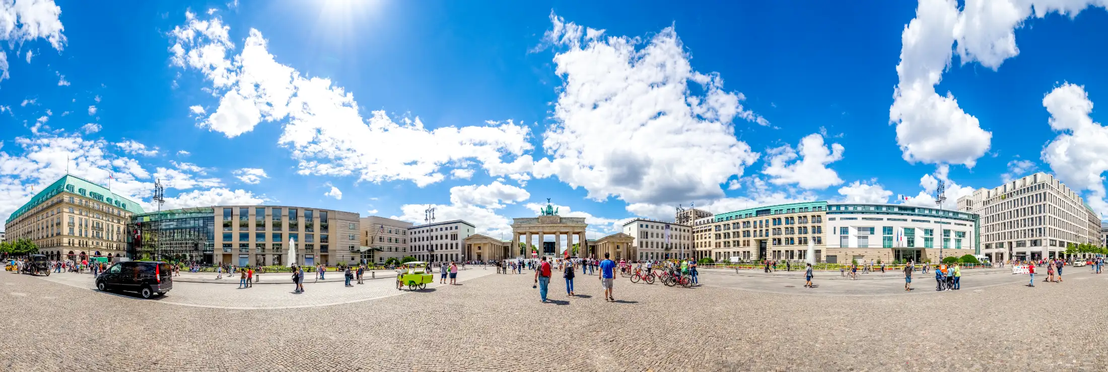 Panoramaaufnahme vom Pariser Platz in Berlin: Links u. a. Hotel Adlon, Akademie der Künste, davor Historischer Springbrunnen, daneben Botschaft der USA, mittig das Brandenburger Tor, rechts u. a. Französische Botschaft und ganz rechts Europäisches Haus