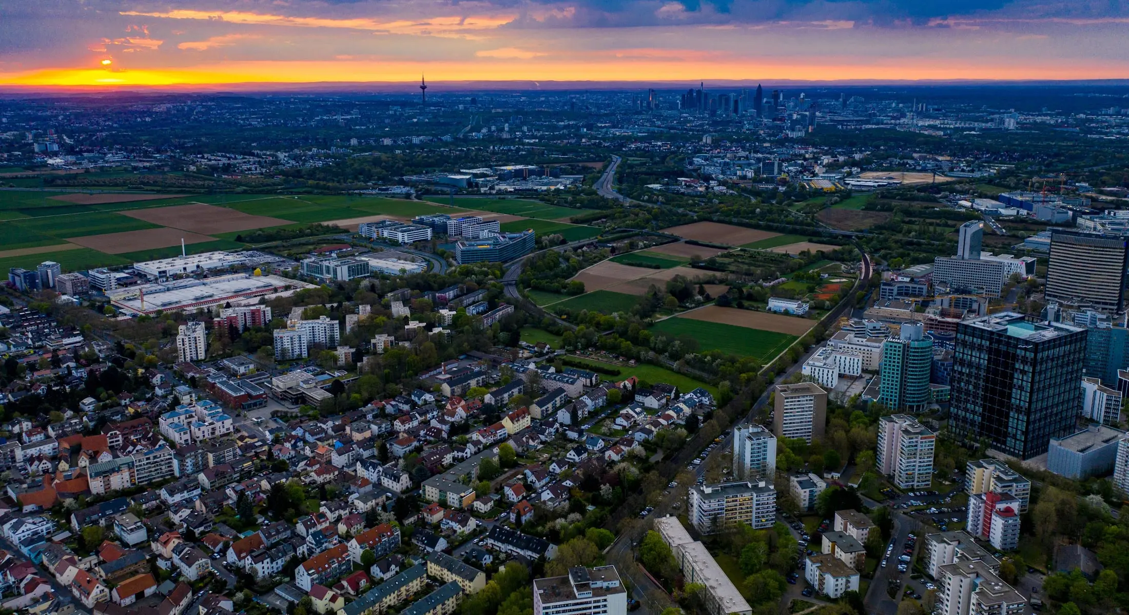 Luftbild von Eschborn bei Sonnenaufgang, im Vordergrund Immobilien in Eschborn, im Hintergrund die Skyline von Frankfurt am Main