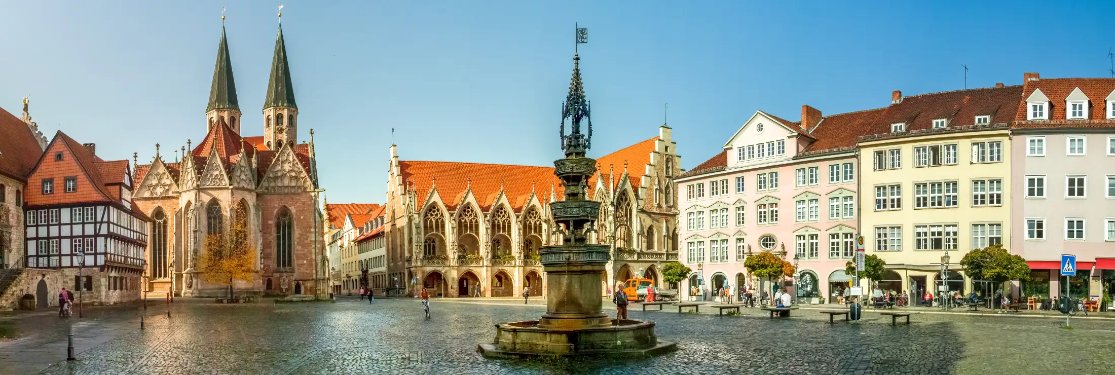 Panoramaaufnahme Braunschweig Altstadtmarkt: im Vordergrund mittig Marienbrunnen, links Immobilien Garküche, rechts daneben St. Martini, mittig Altstadtrathaus (leicht verdeckt durch Marienbrunnen), rechts weitere Immobilien Altstadtmarkt