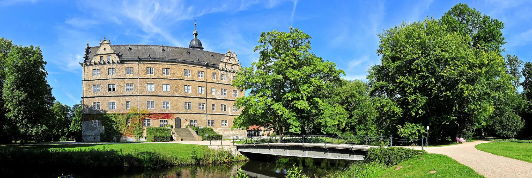 Schloss Wolfsburg von Osten; zu sehen ist der Ostflügel mit der Freitreppe und Teile des Schlossgartens an einem Sommertag