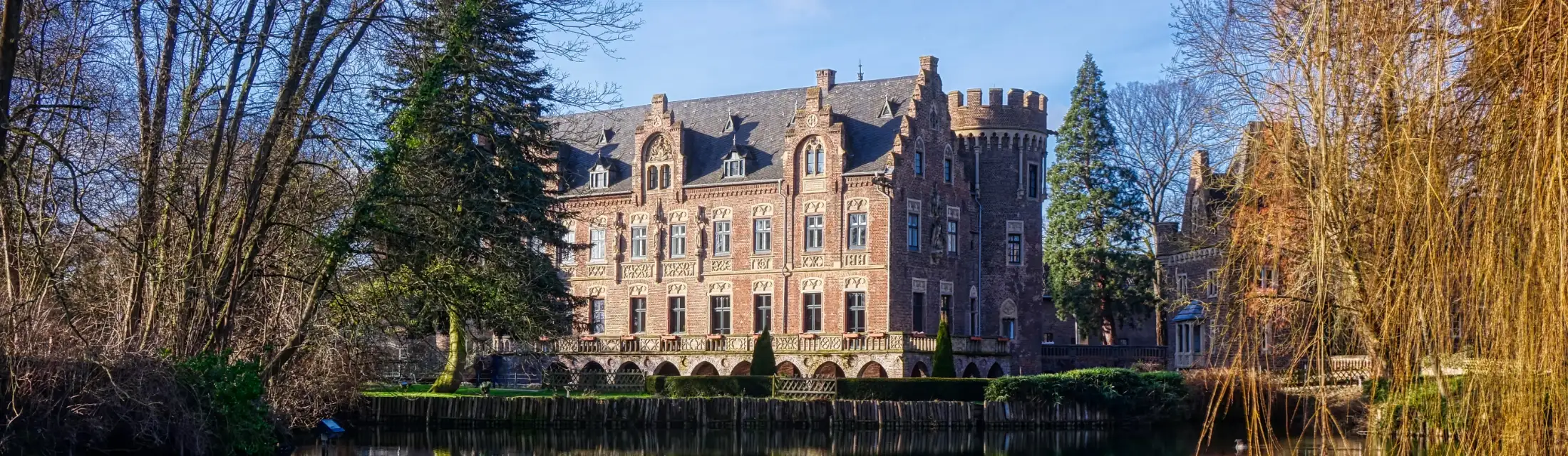 Schloss Paffendorf, ein Wasserschloss: im Vordergrund der Wassergraben, links und rechts herbstliche Bäume des Schlossgartens, mittig Schloss Paffendorf Nordseite.