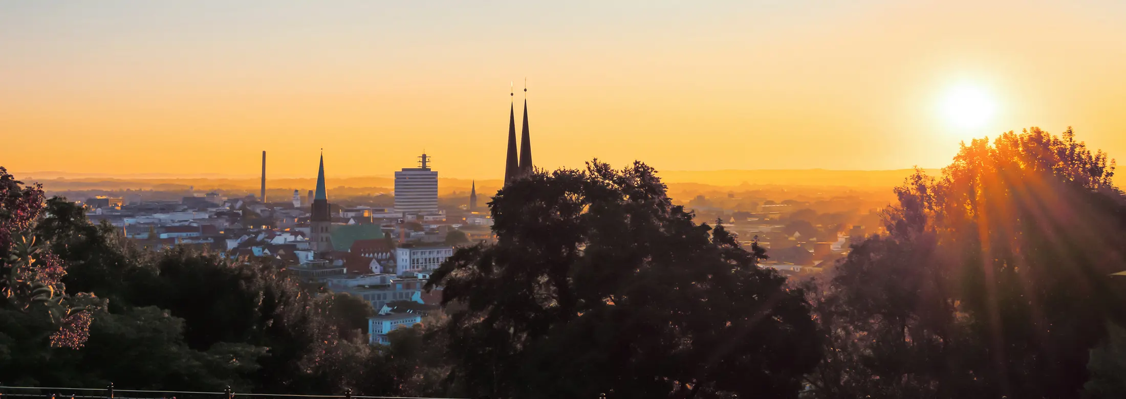 Blick auf Bielefeld von der Sparrenburg Richtung Nordosten nach Bielefeld Mitte mit der Neustädter Marienkirche mittig, links davon das Telekom-Hochhaus und rechts die aufgehende Sonne