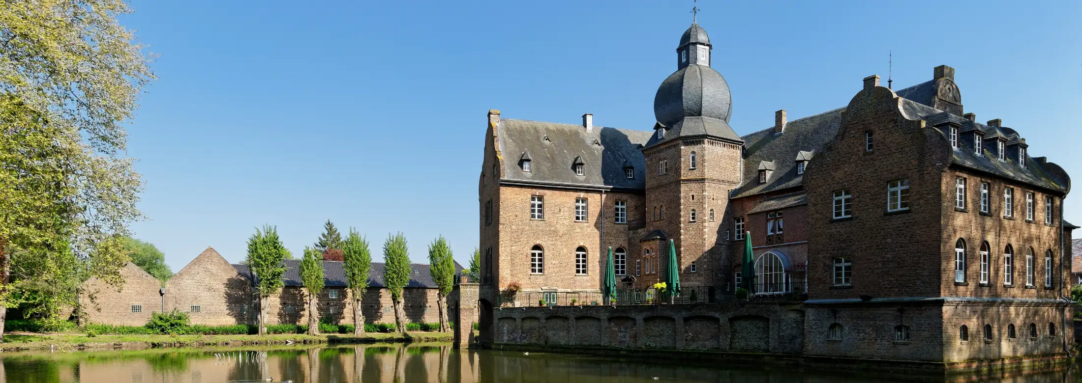 Die Wasserburg Burg Bergerhausen in Kerpen Blatzheim von Norden: vorne Wassergraben, links Immobilien Wasserburg, mittig bis rechts die Burganlage an einem Sommertag