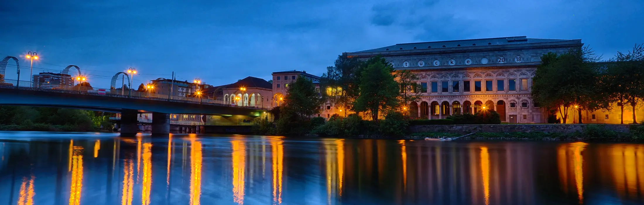 Mülheim an der Ruhr in der Dämmerung mit der Stadthalle und der Schloßbrücke über die Ruhr, in der sich die Lichter spiegeln