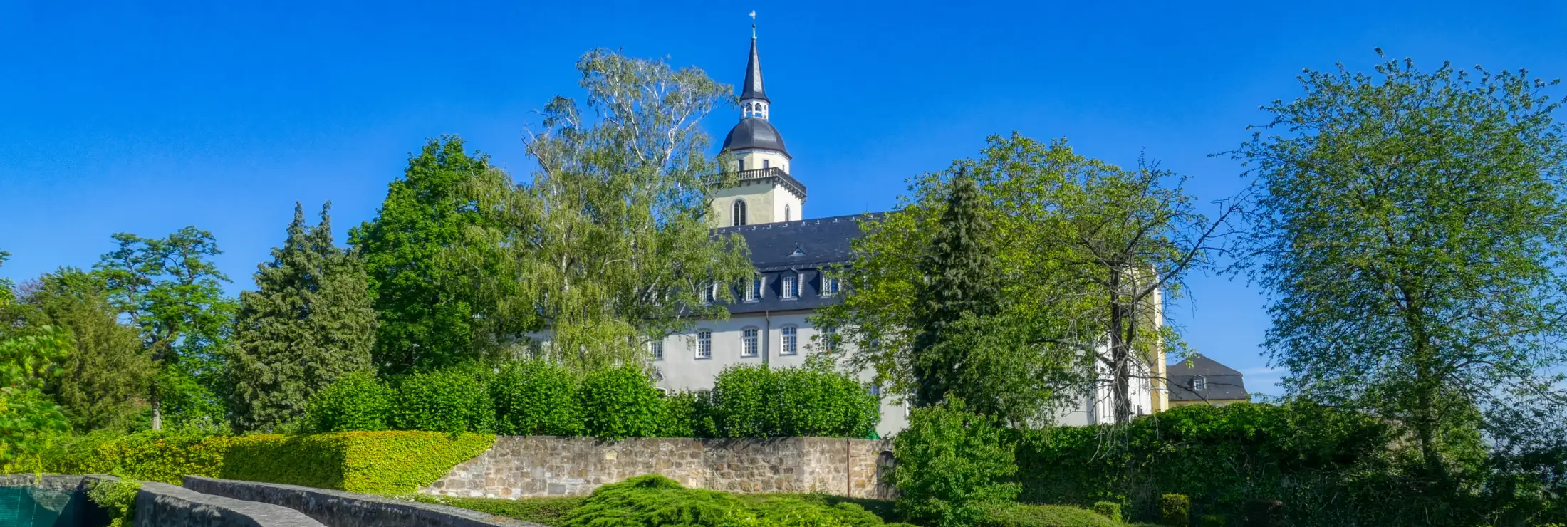 Die Abtei St. Michael auf dem Michaelsberg, eine ehemalige Benediktinerabtei und das Wahrzeichen der Stadt Siegburg. Aufgenommen von Süden, aus dem Johannesgarten an einem Sommertag.