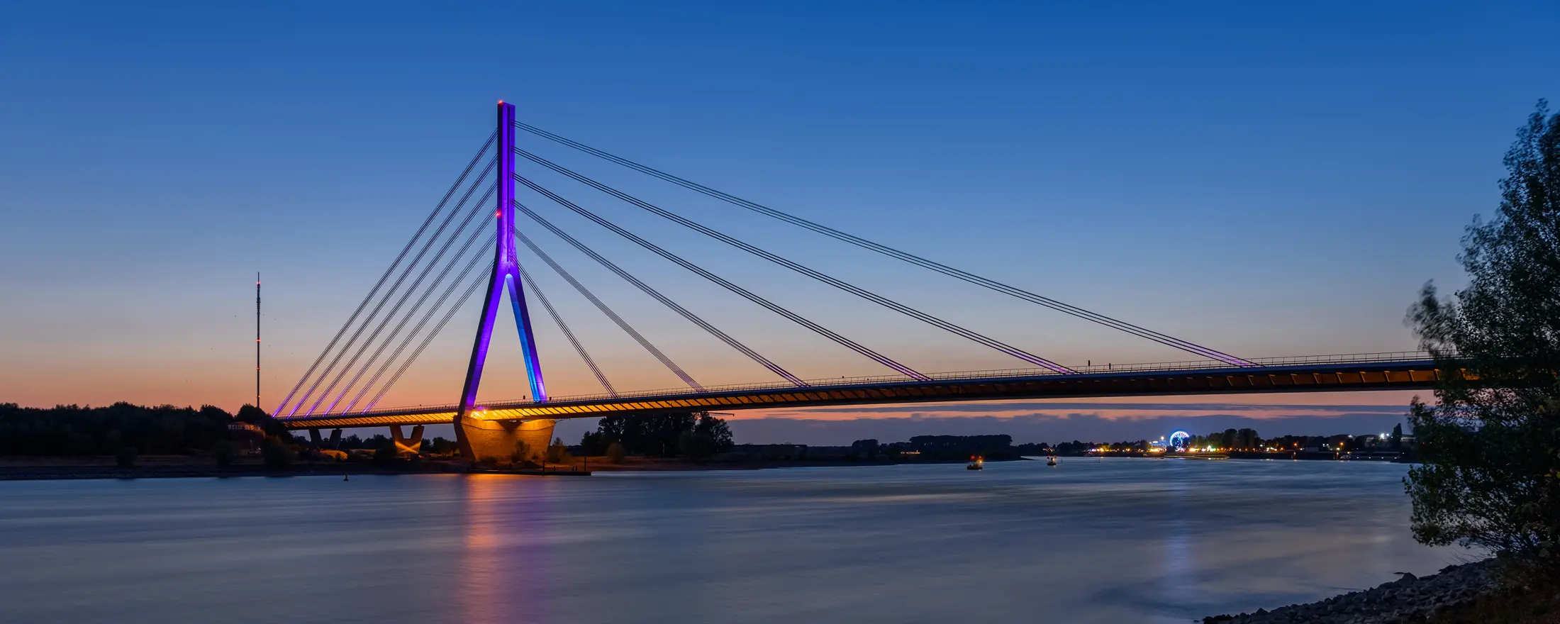 Ansicht der beleuchteten Rheinbrücke im Süden von Wesel in der Dämmerung, mit Zitadellenviertel und den dortigen Immobilien im Hintergrund