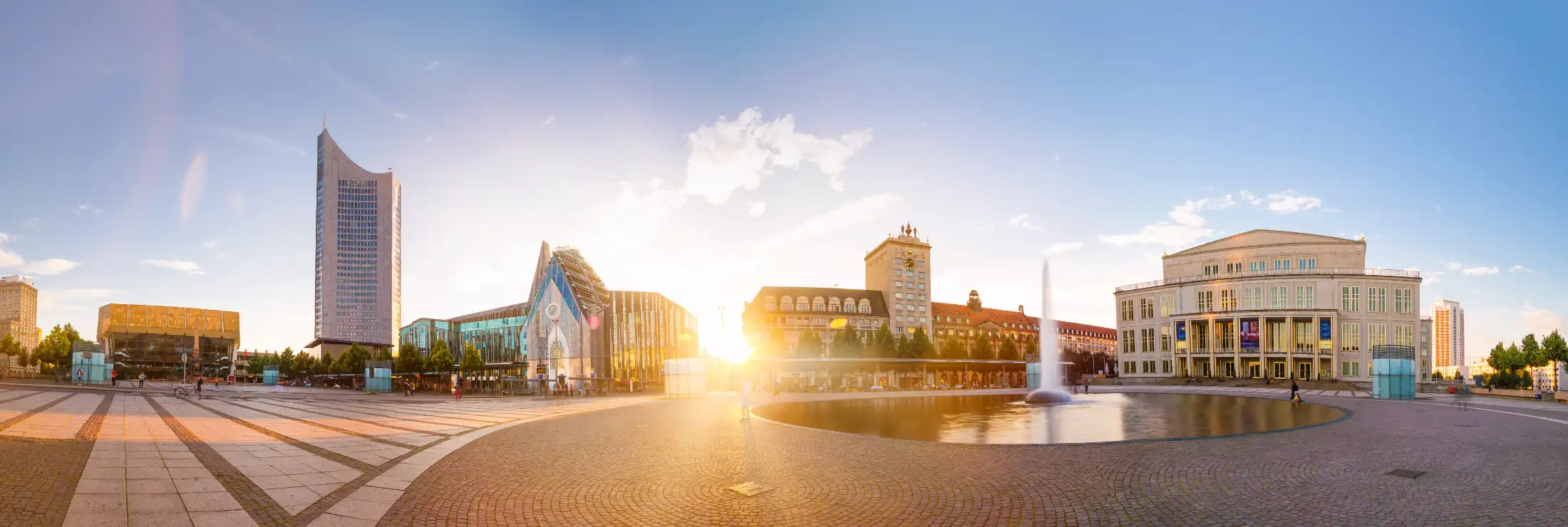 Panoramaaufnahme vom Augustusplatz: links das Gewandhaus, der Mendebrunnen davor, daneben MDR-Kubus und Paulinum, Bildmitte Grimmaische Straße mit untergehender Sonne, daneben Ägyptisches Museum, rechts die Oper, der Opernbrunnen davor.